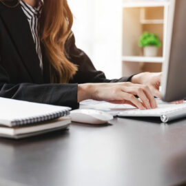 Happy businesswoman wearing suit posing sitting in a desktop at office workspace.
